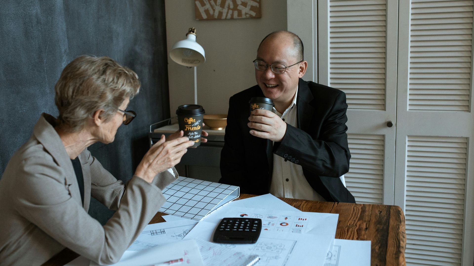 Two business colleagues collaborating over coffee inside a cozy workspace, smiling and discussing ideas.