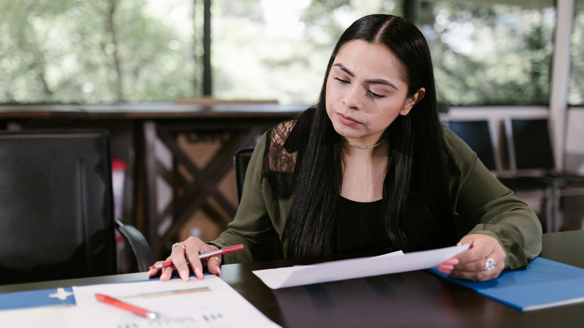Professional woman in office setting studying documents with concentration.