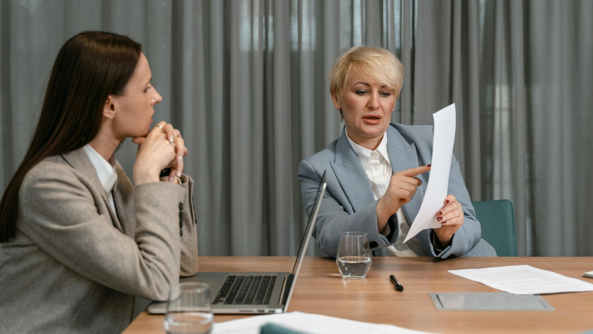 Two businesswomen discussing documents during a professional meeting around a conference table.