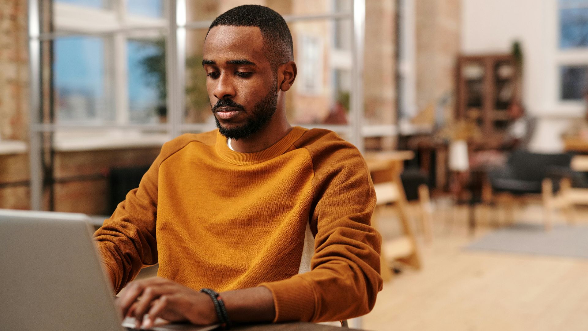 A focused man in a sweater working on his laptop in a modern office setting. Perfect for business and technology themes.