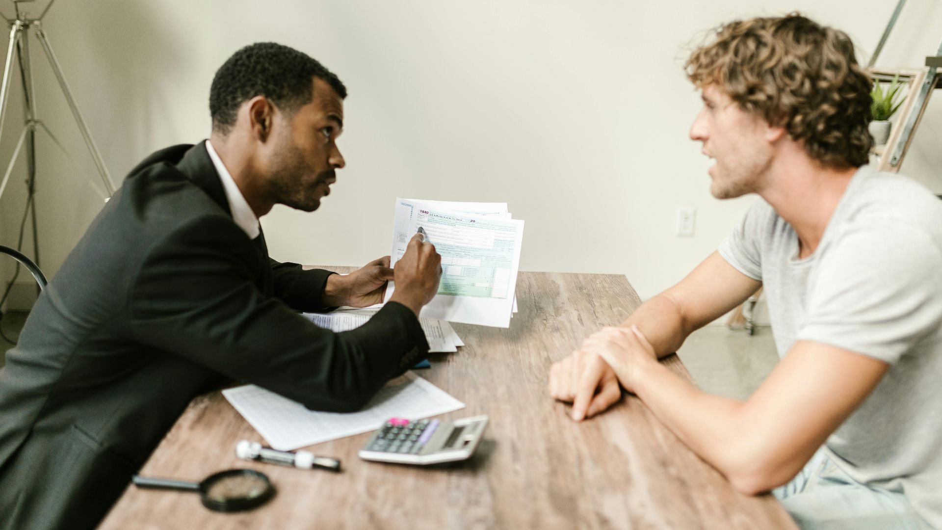 A financial advisor discusses paperwork with a client at a desk in a modern office.