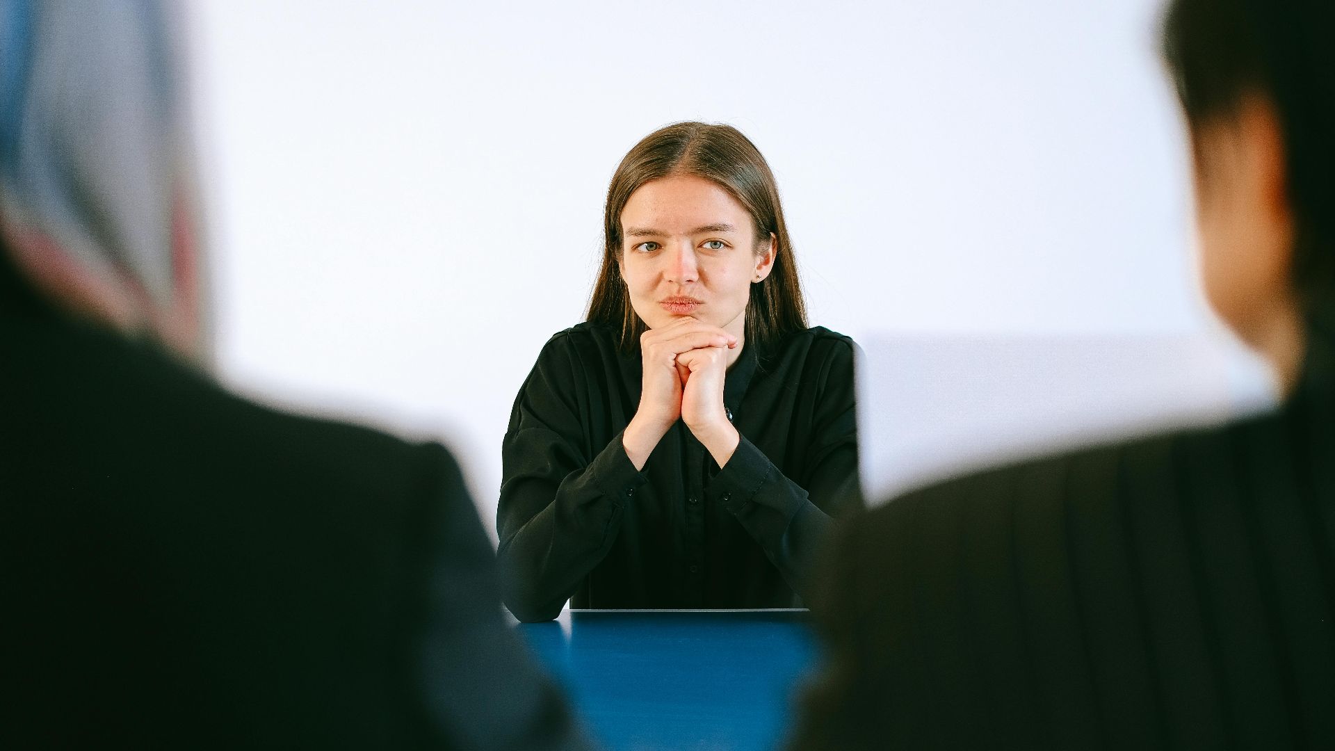 A woman in a job interview facing two people at an office table, focusing intently.