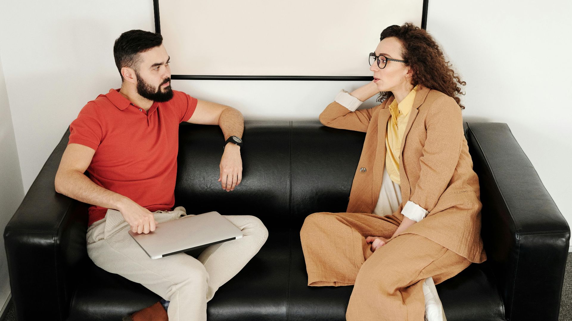 A man and woman sit on a black sofa, having a professional conversation.
