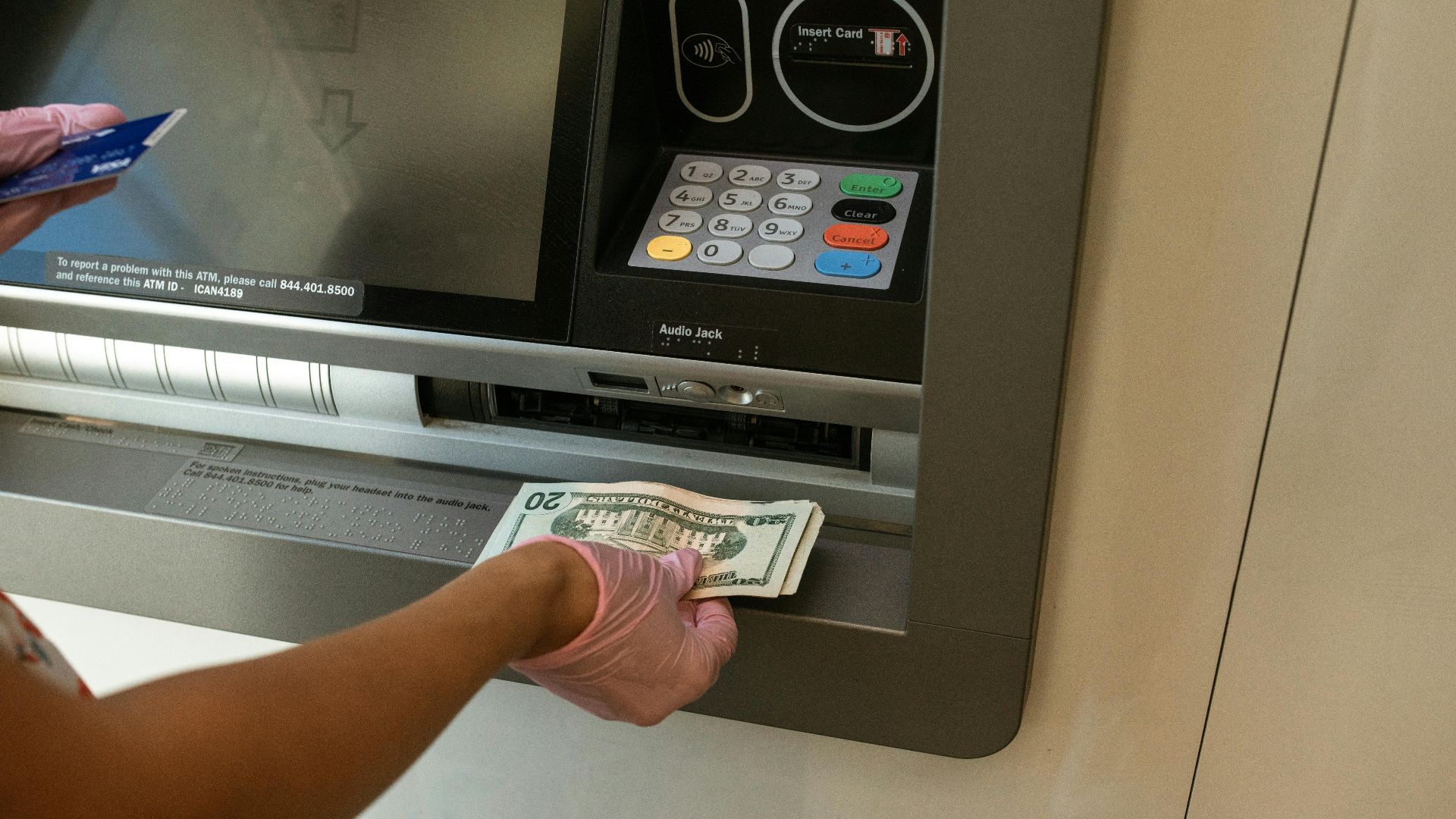 A person wearing gloves withdrawing cash from an ATM machine showcasing money handling and hygiene.