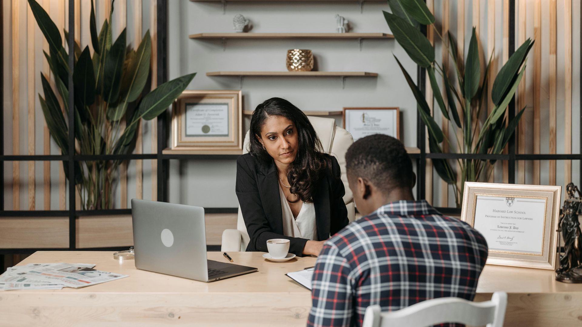 Two professionals engaged in discussion in a modern office with certificates and plants.