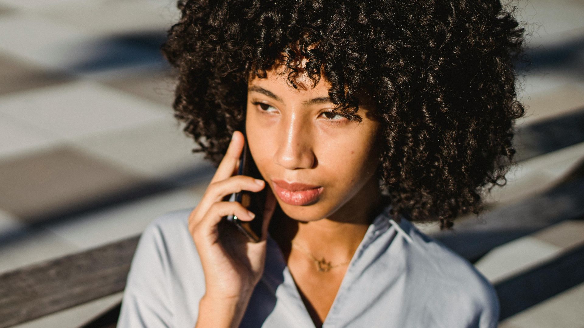 Casual chic woman outdoors talking on cellphone and holding coffee.