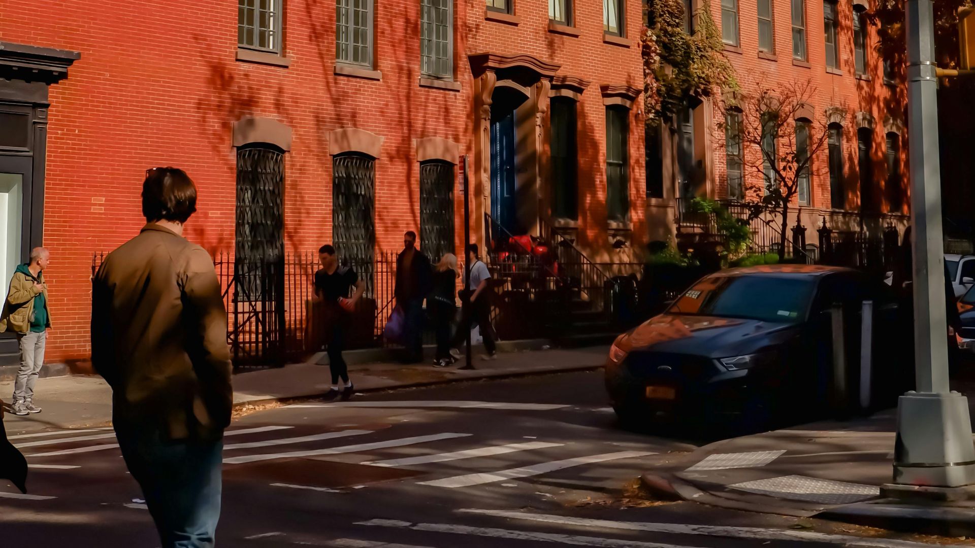 Pedestrian walking past red brick residential buildings on a sunny day in New York City.