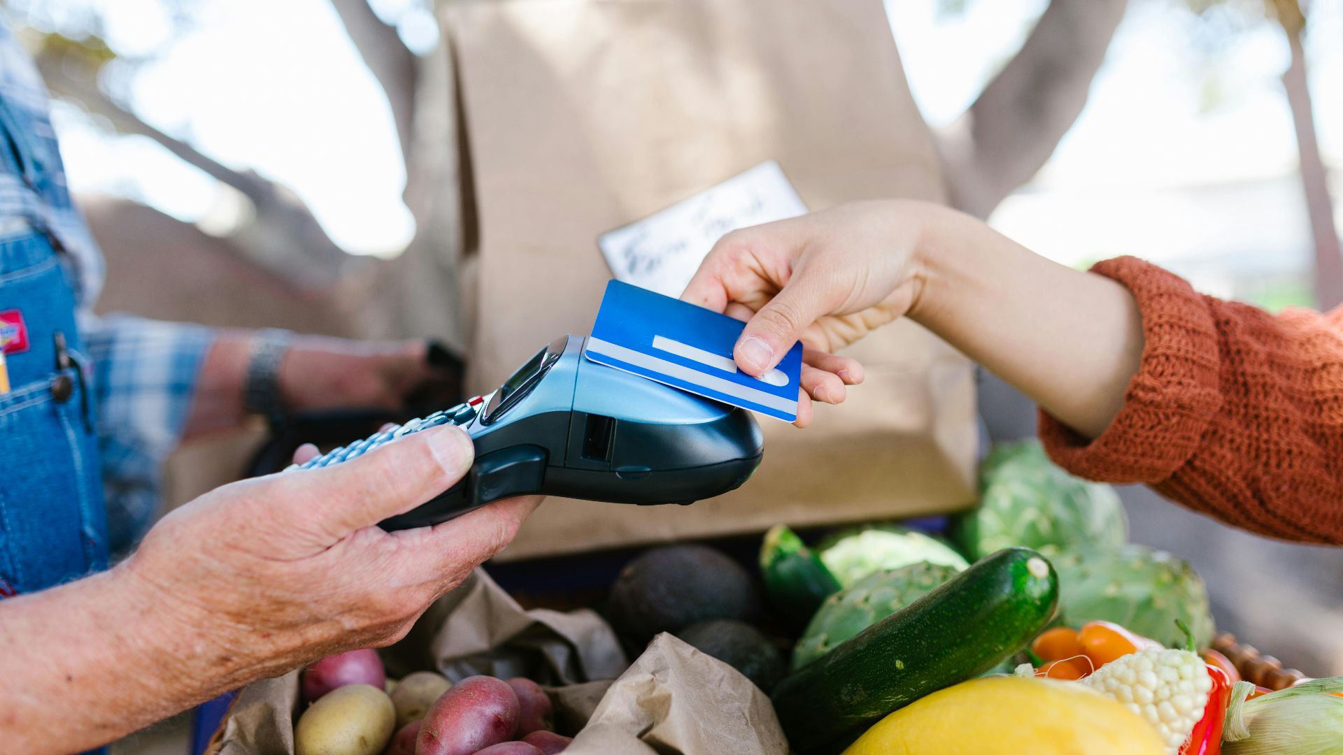 A customer making a contactless payment with a credit card at a farmers market.