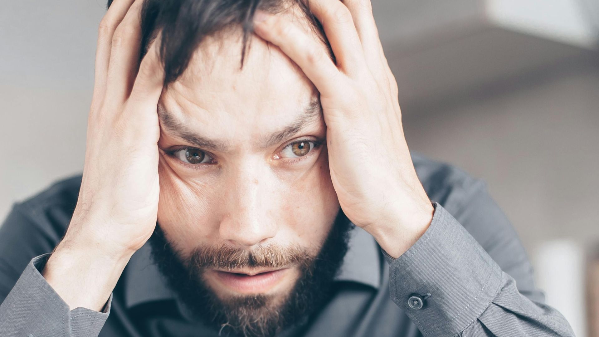 Man with hands on head looking stressed and frustrated indoors.