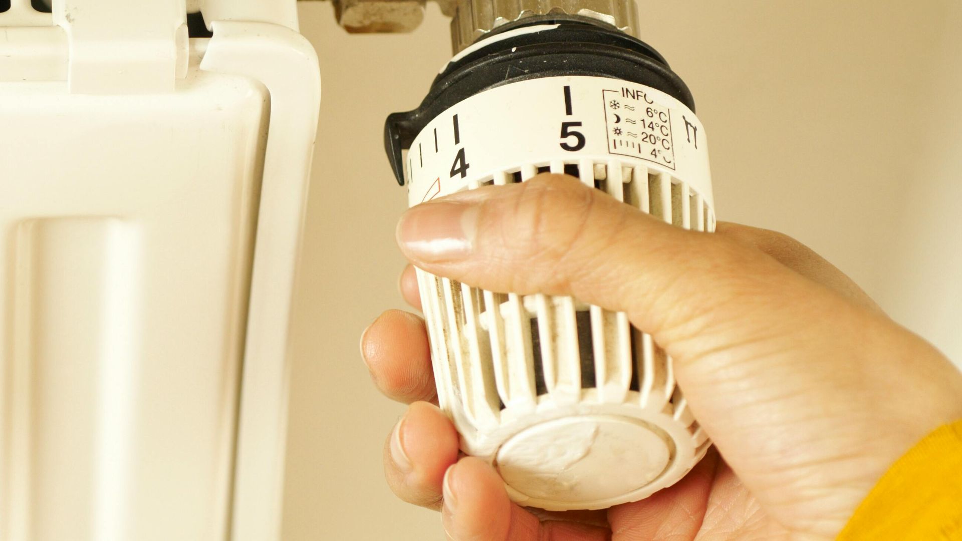 Close-up of hand adjusting radiator thermostat to control home heating temperature.