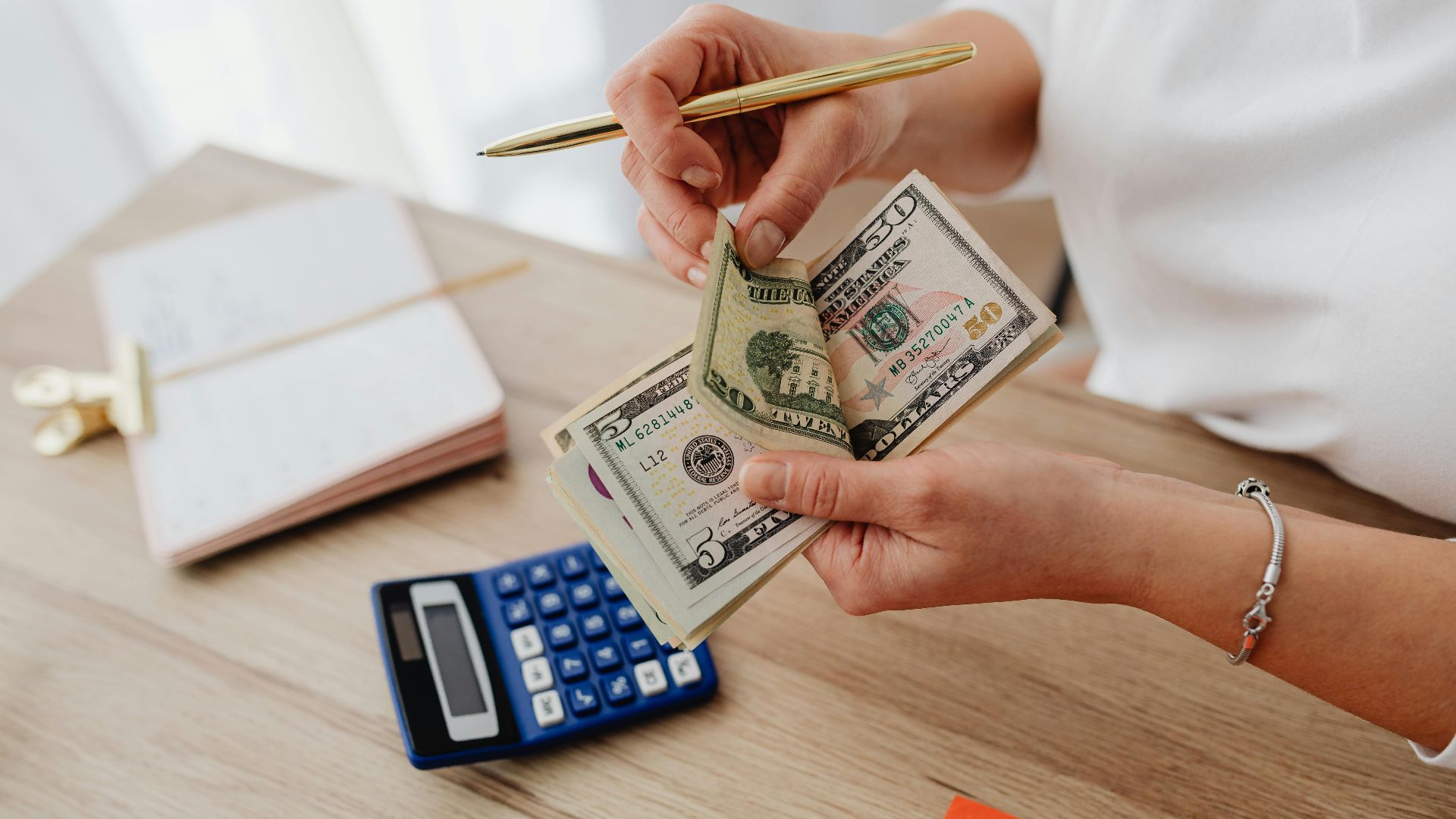 Woman counting cash with a calculator at a desk, managing finances.