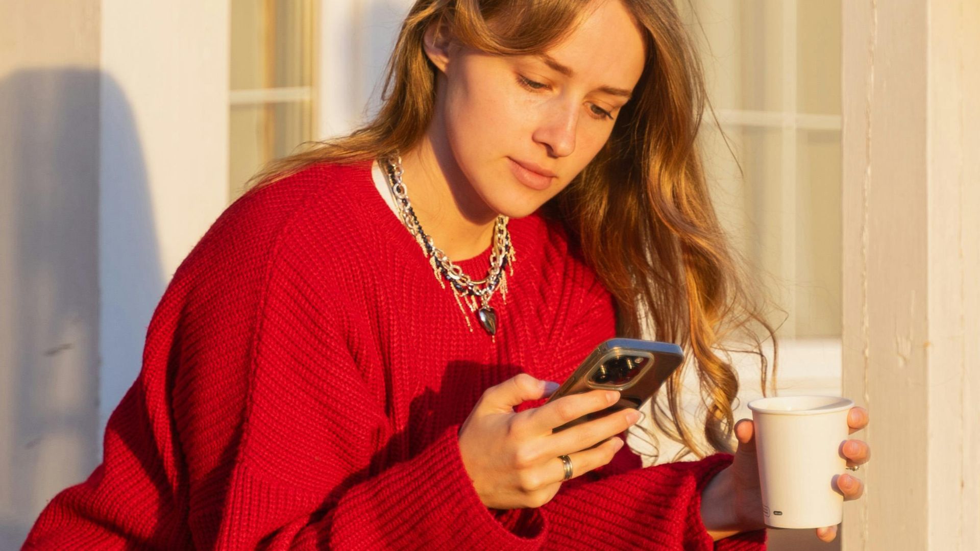 A woman in a red sweater and sneakers sits on wooden stairs, enjoying sunset light.