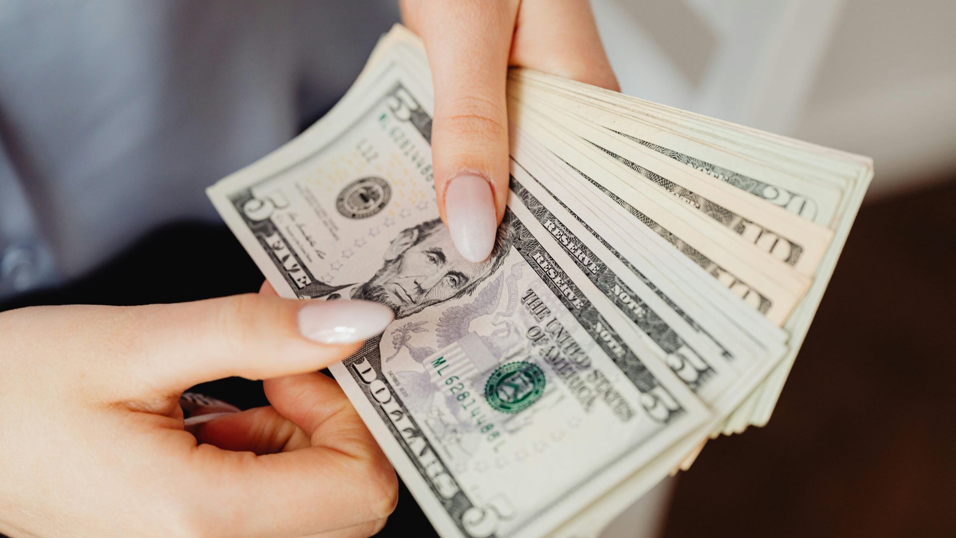 Hands count US dollar bills, showcasing finance and cash handling concepts.