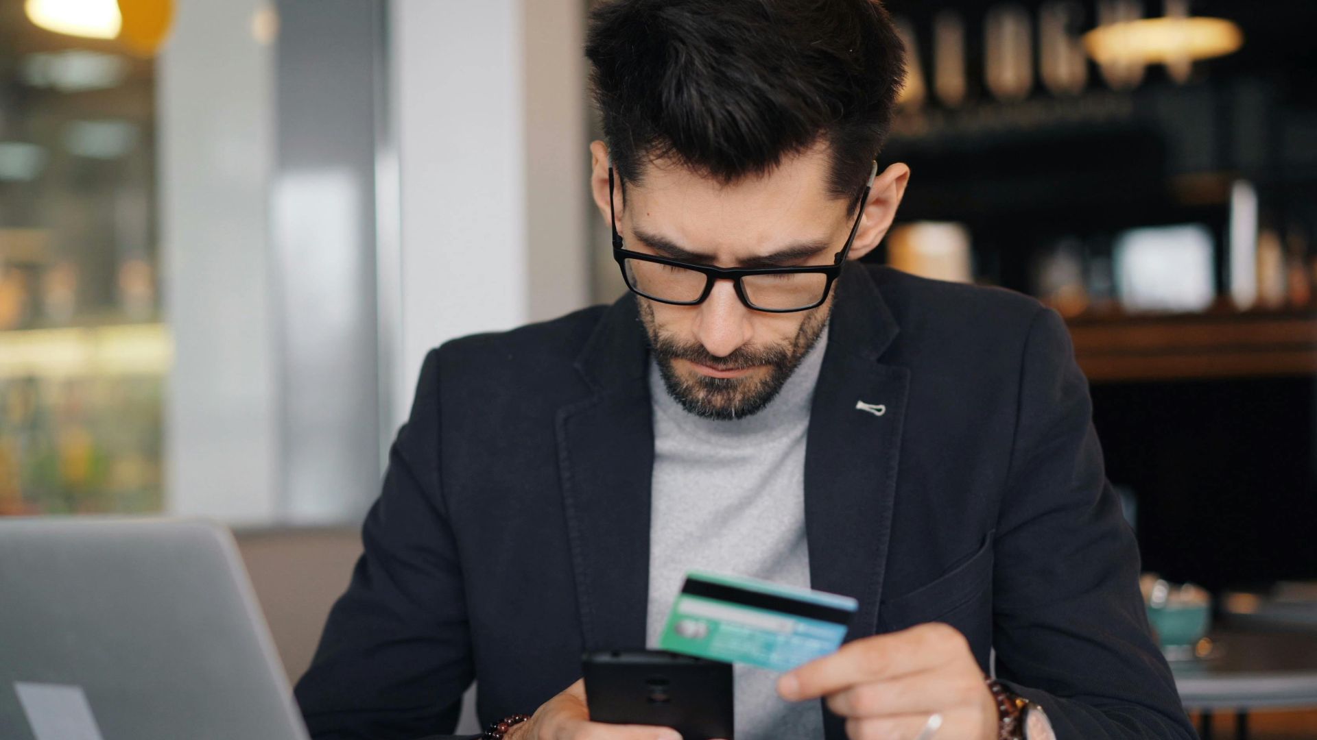 Businessman making online payment with smartphone and credit card in a modern café.