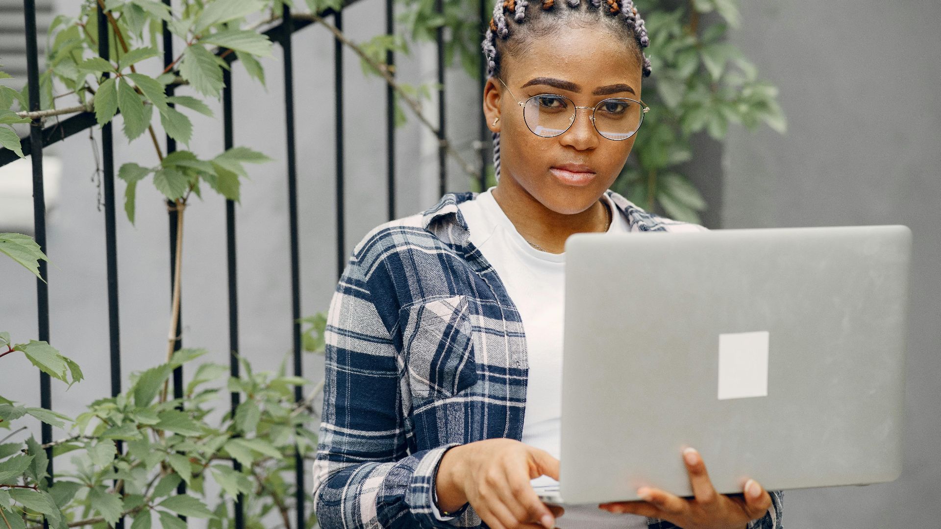 Confident young woman with braided hair using a laptop outdoors.