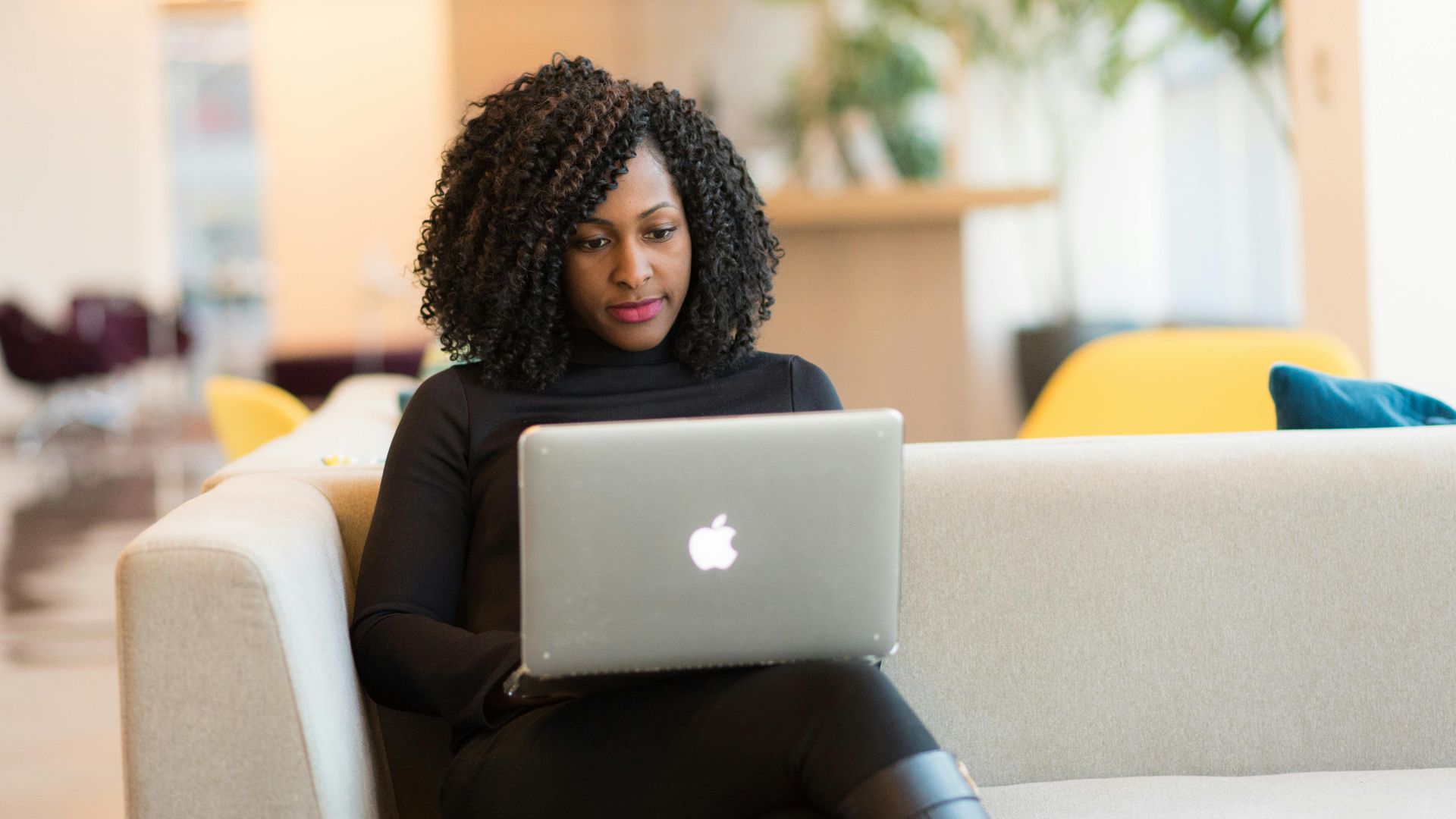 An African American woman working remotely on a laptop in a modern indoor setting.