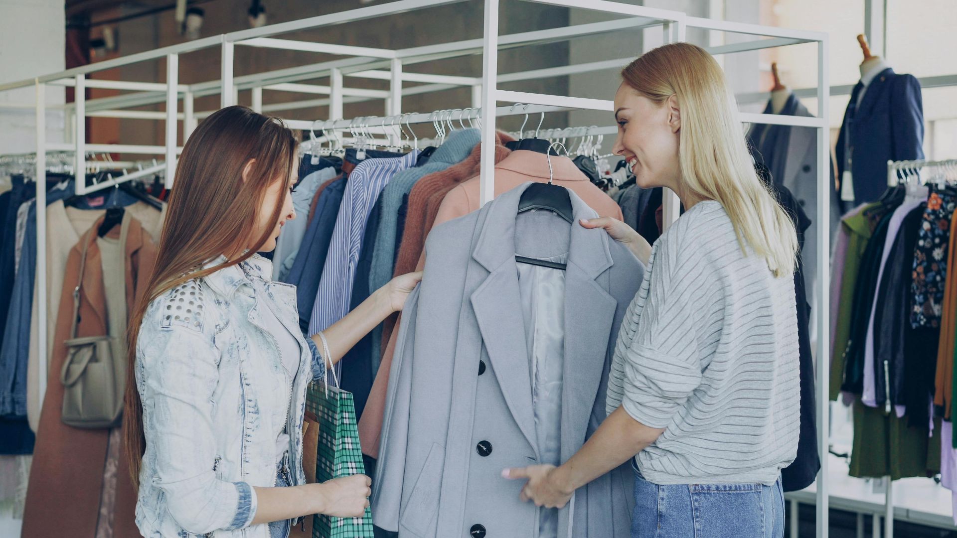 Two women shopping in a clothing store, examining a stylish gray blazer on a rack.