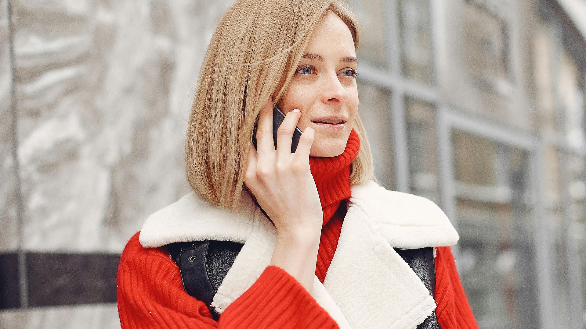 Woman in a vibrant red sweater and black vest talking on the phone outdoors.