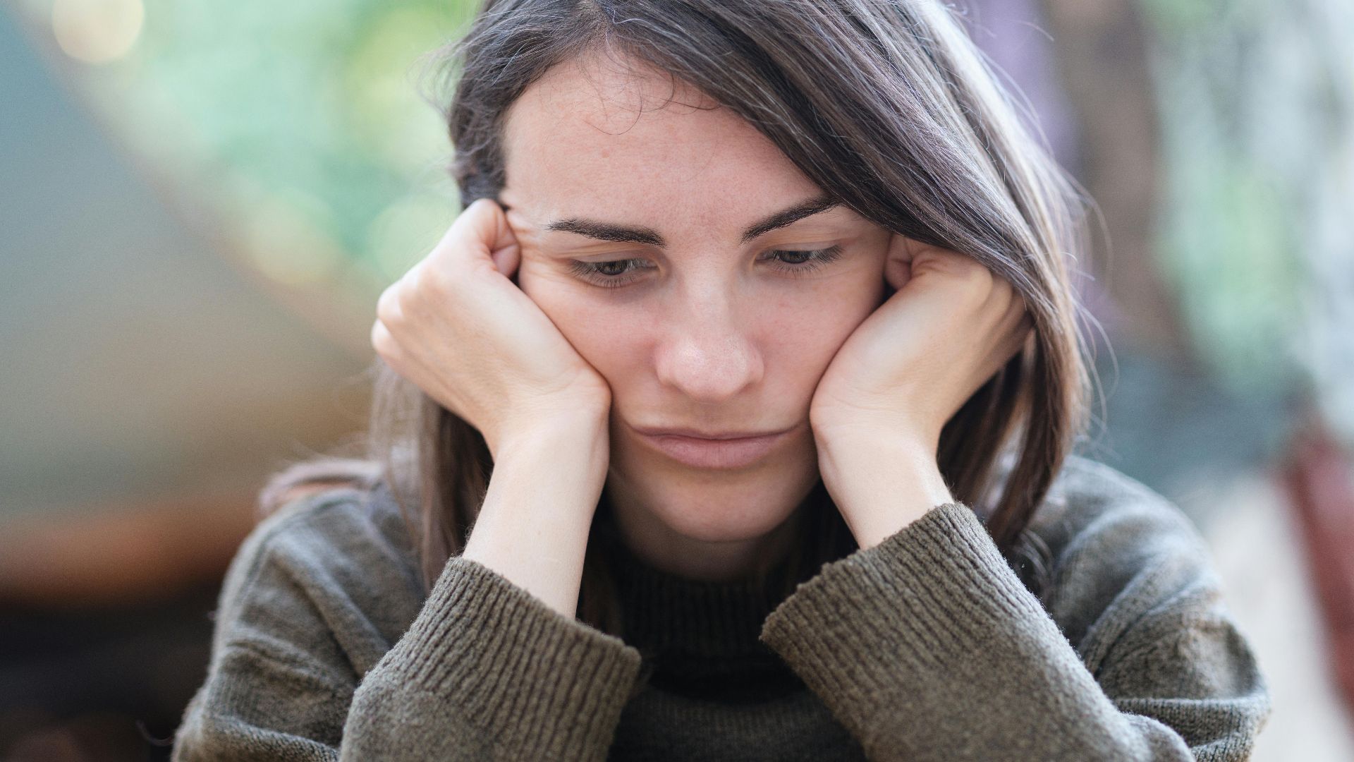 Portrait of a young woman looking pensive and thoughtful while sitting outdoors.