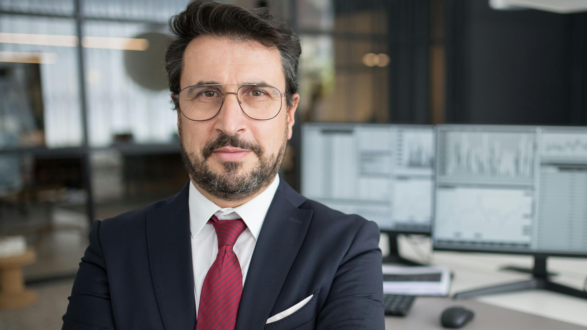 Business professional in corporate attire with arms crossed in a modern office space.