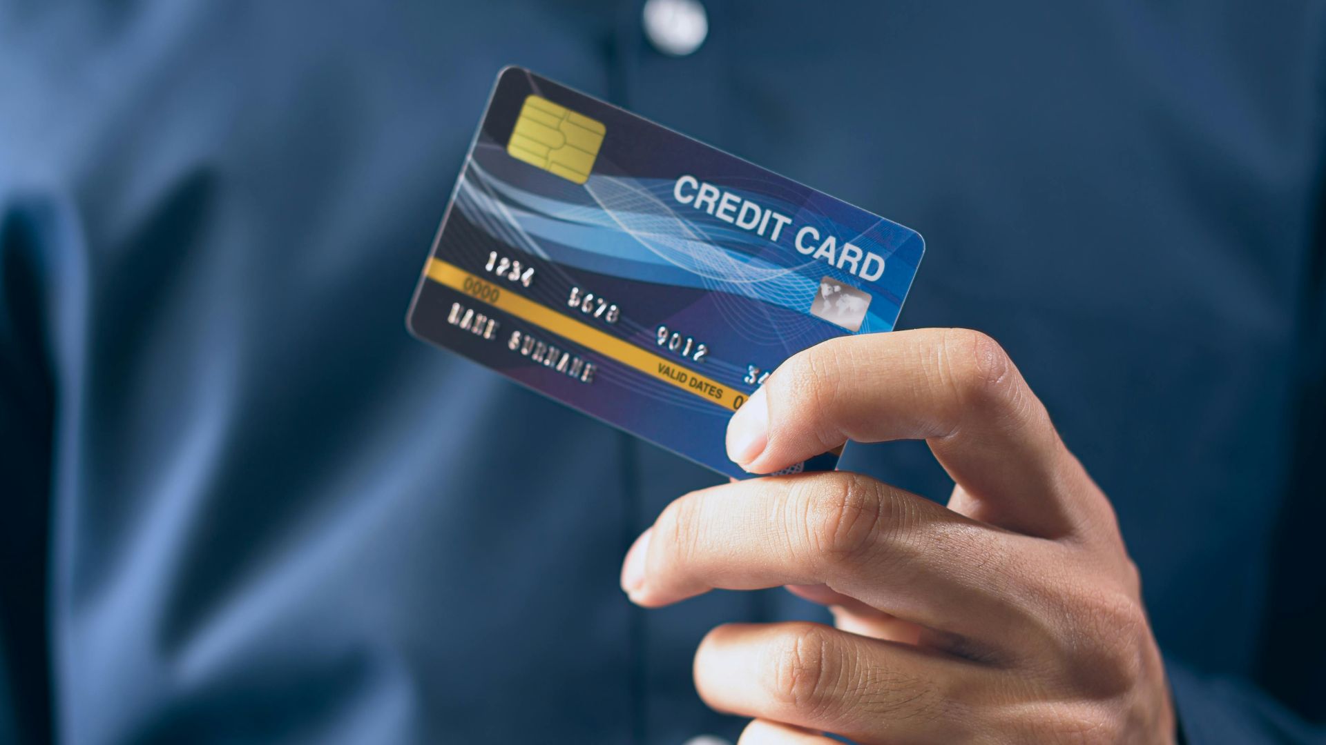 Close-up of a person holding a credit card in a hand, wearing a button-up shirt.