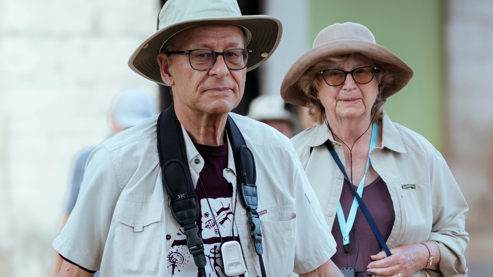 Elderly couple with sun hats and cameras crossing a zebra crossing outdoors.