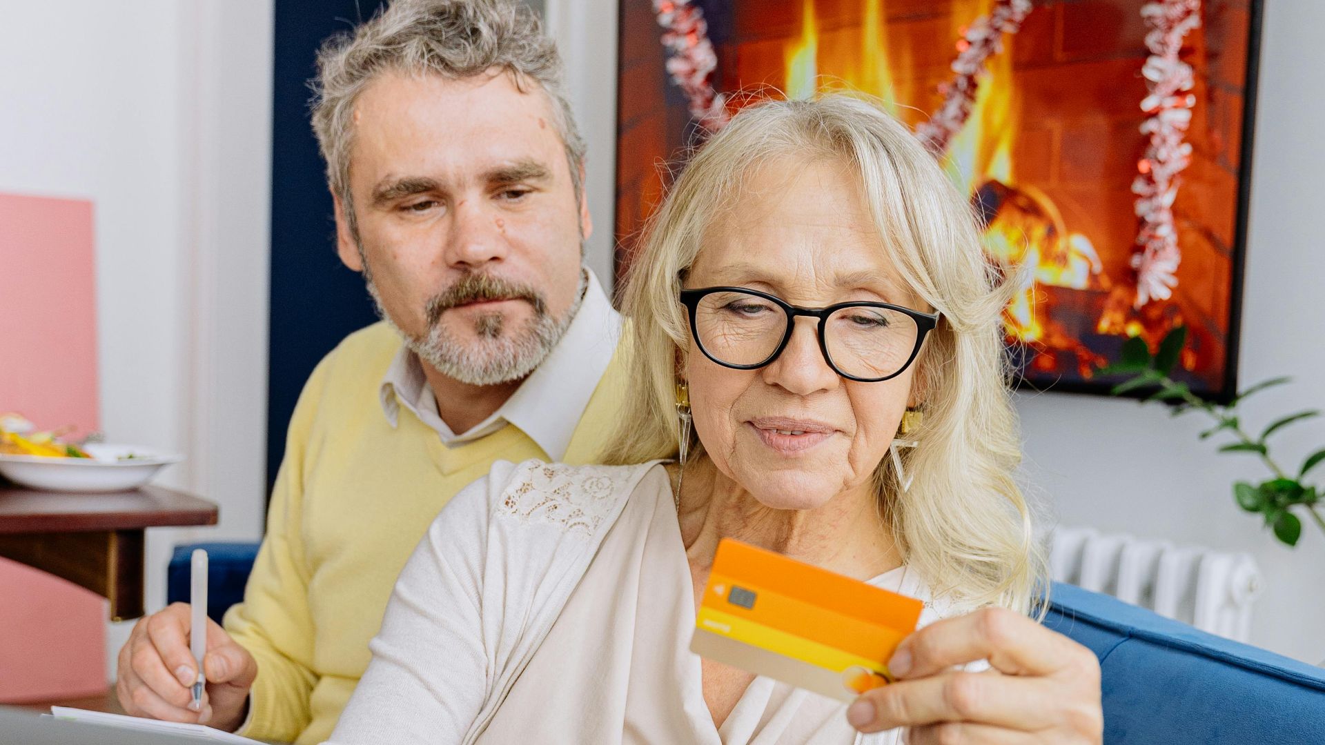 Elderly couple smiles as they shop online with a credit card on a cozy couch.