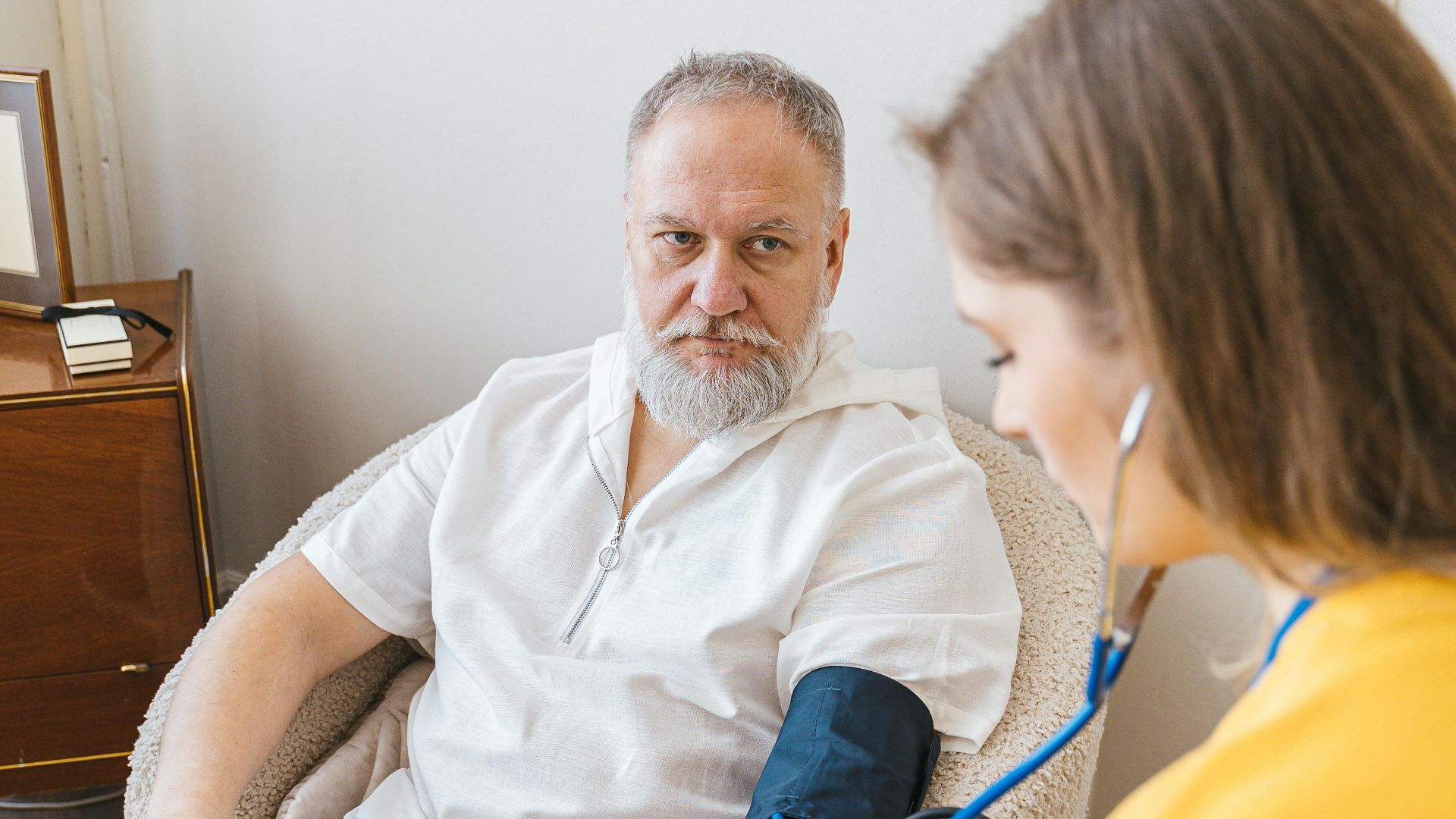 An elderly man having his blood pressure checked by a nurse during a routine health checkup indoors.