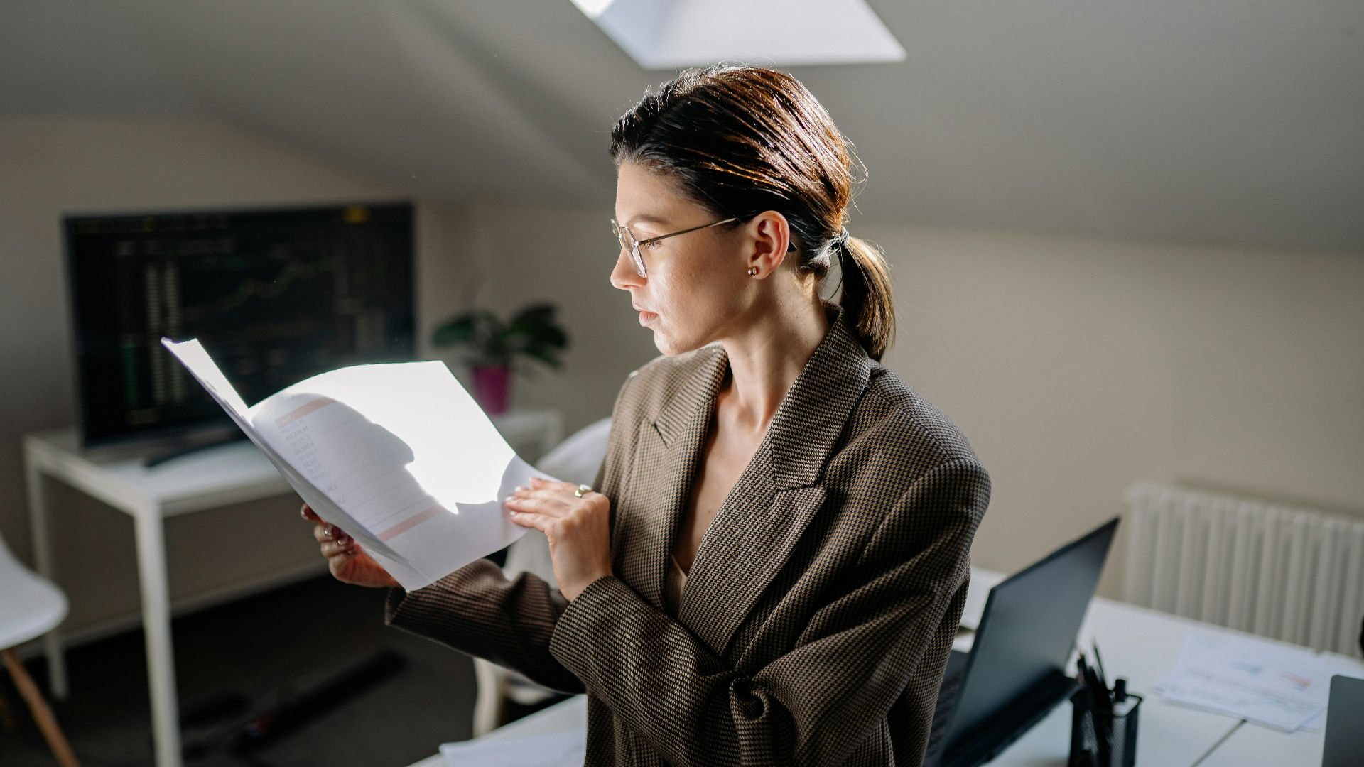 Professional woman in glasses reviewing financial documents at her office desk.