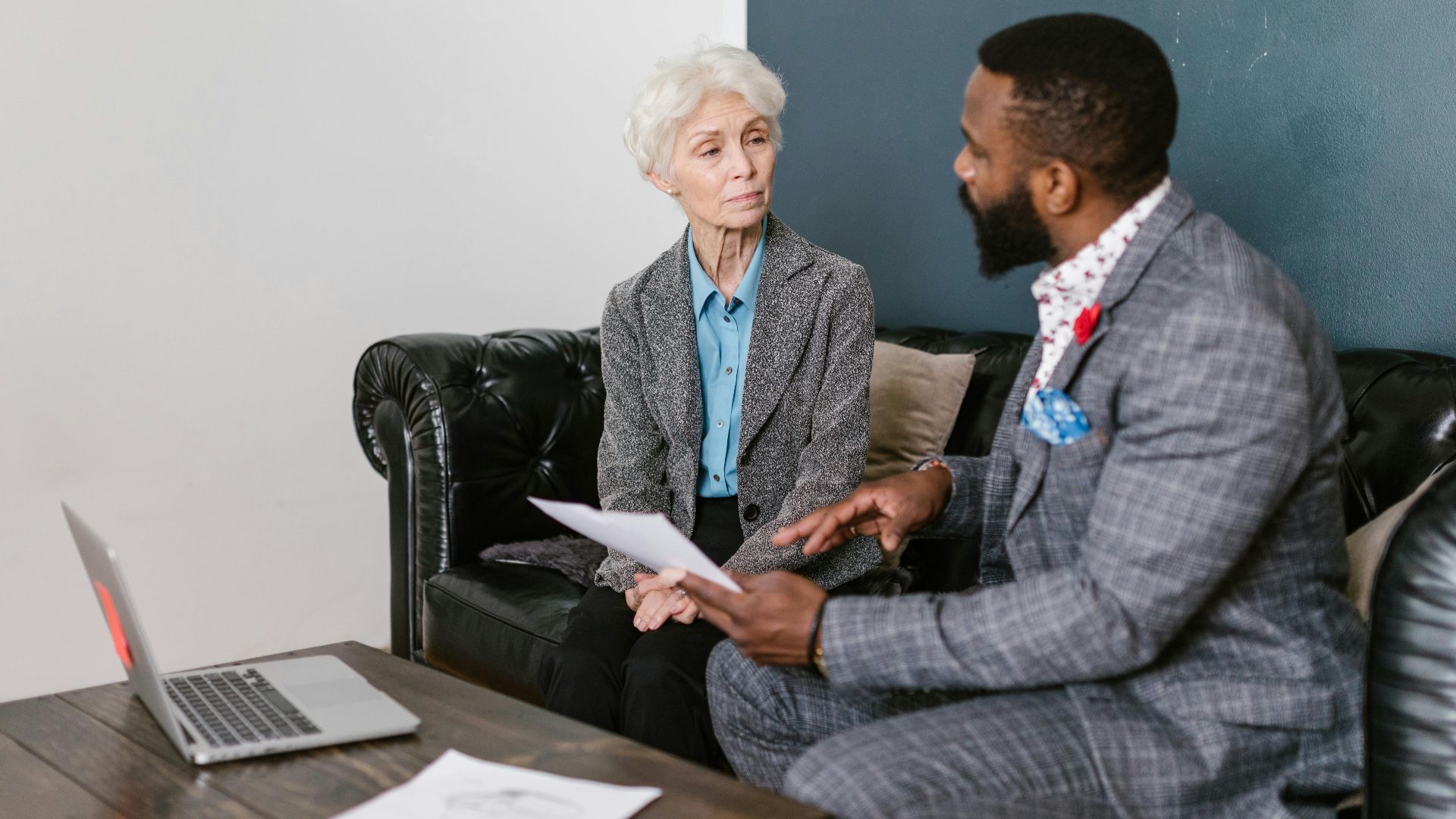 An elderly woman and a man in a professional meeting discussing documents indoors.