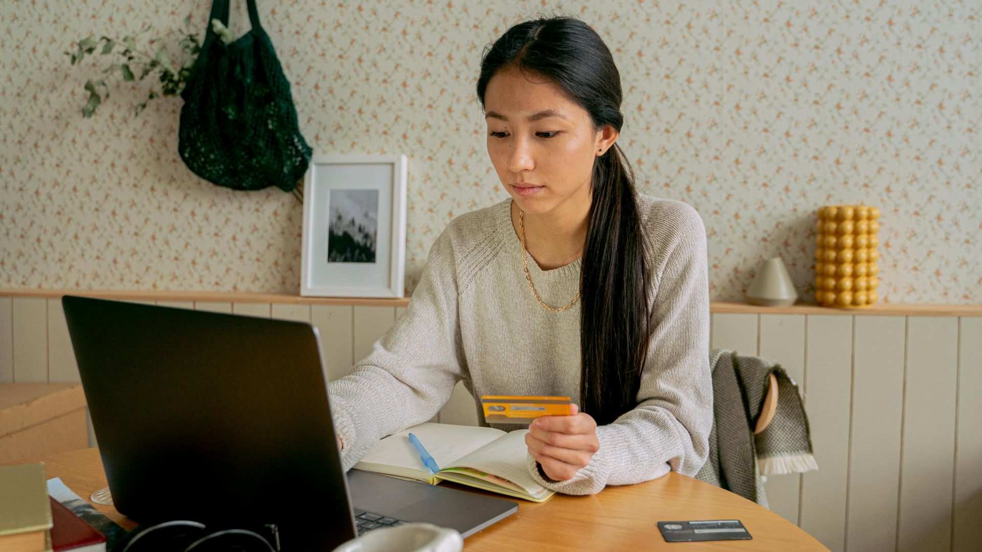 A woman using a laptop and credit card for online shopping at a cozy indoor setting.