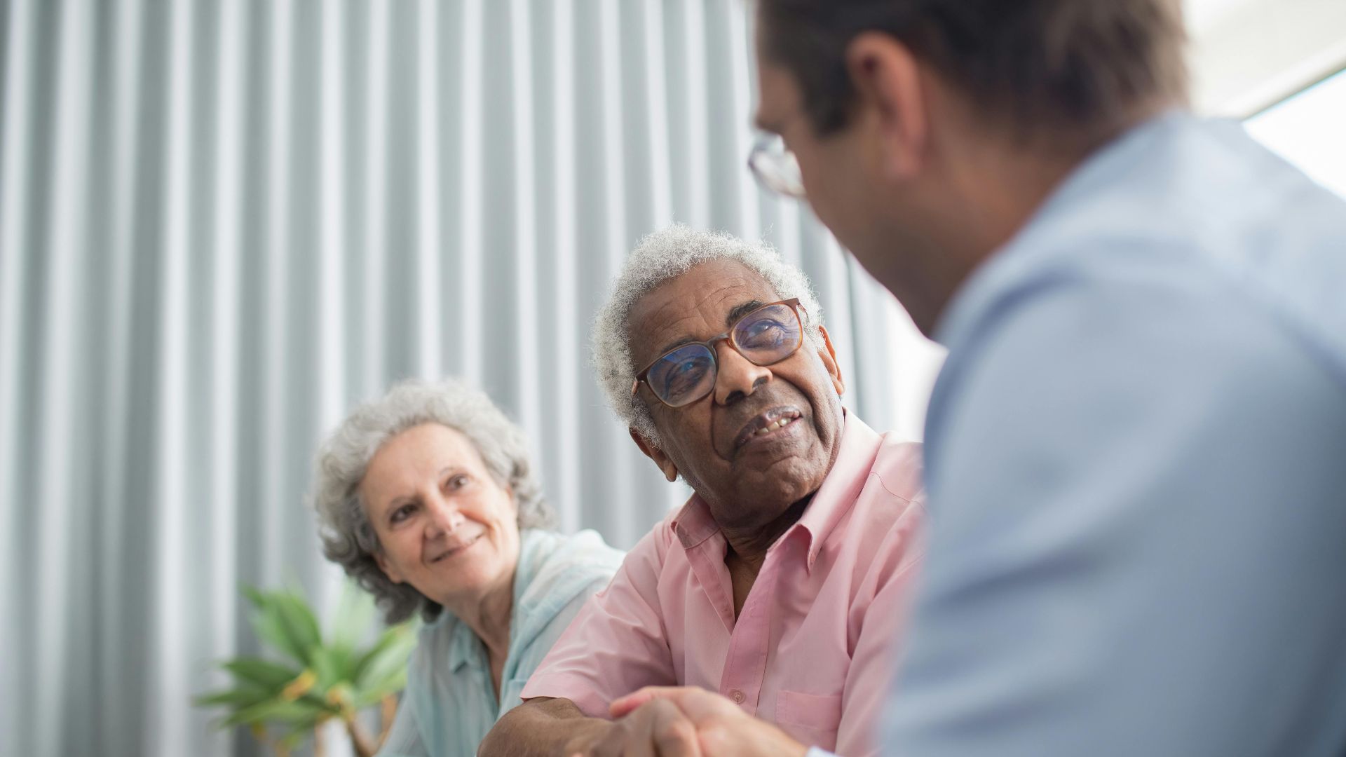 Elderly couple discussing with a consultant indoors, expressing interest and connection.
