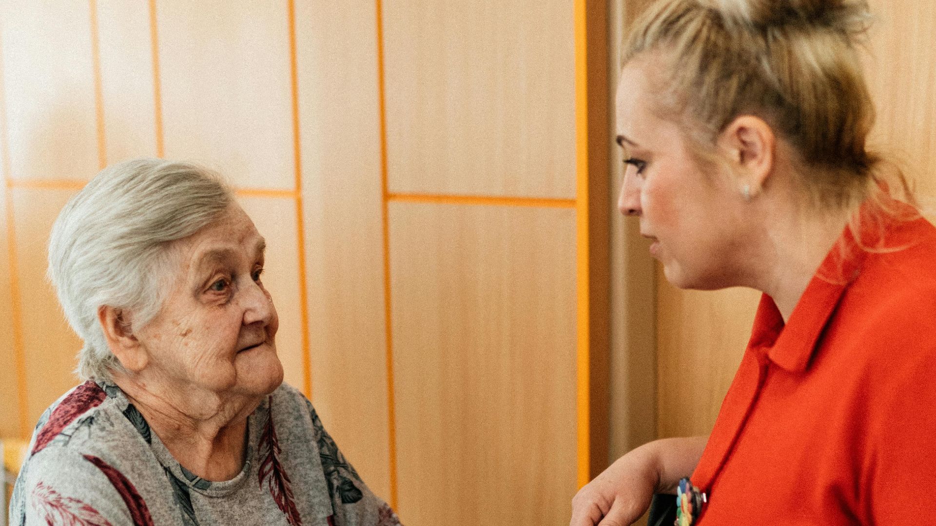 A caregiver assists an elderly woman in a retirement home corridor, fostering companionship and support.