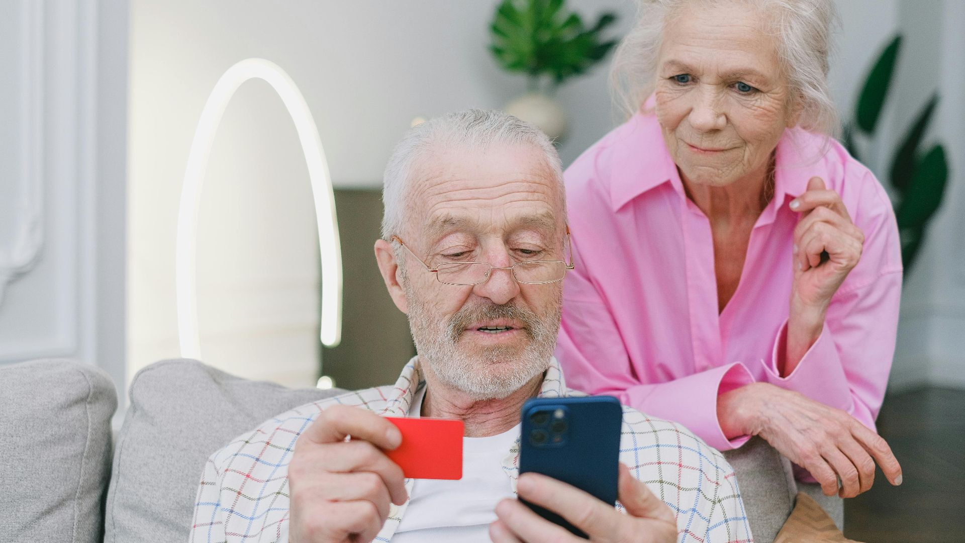 Elderly couple using smartphone and credit card for online shopping at home.
