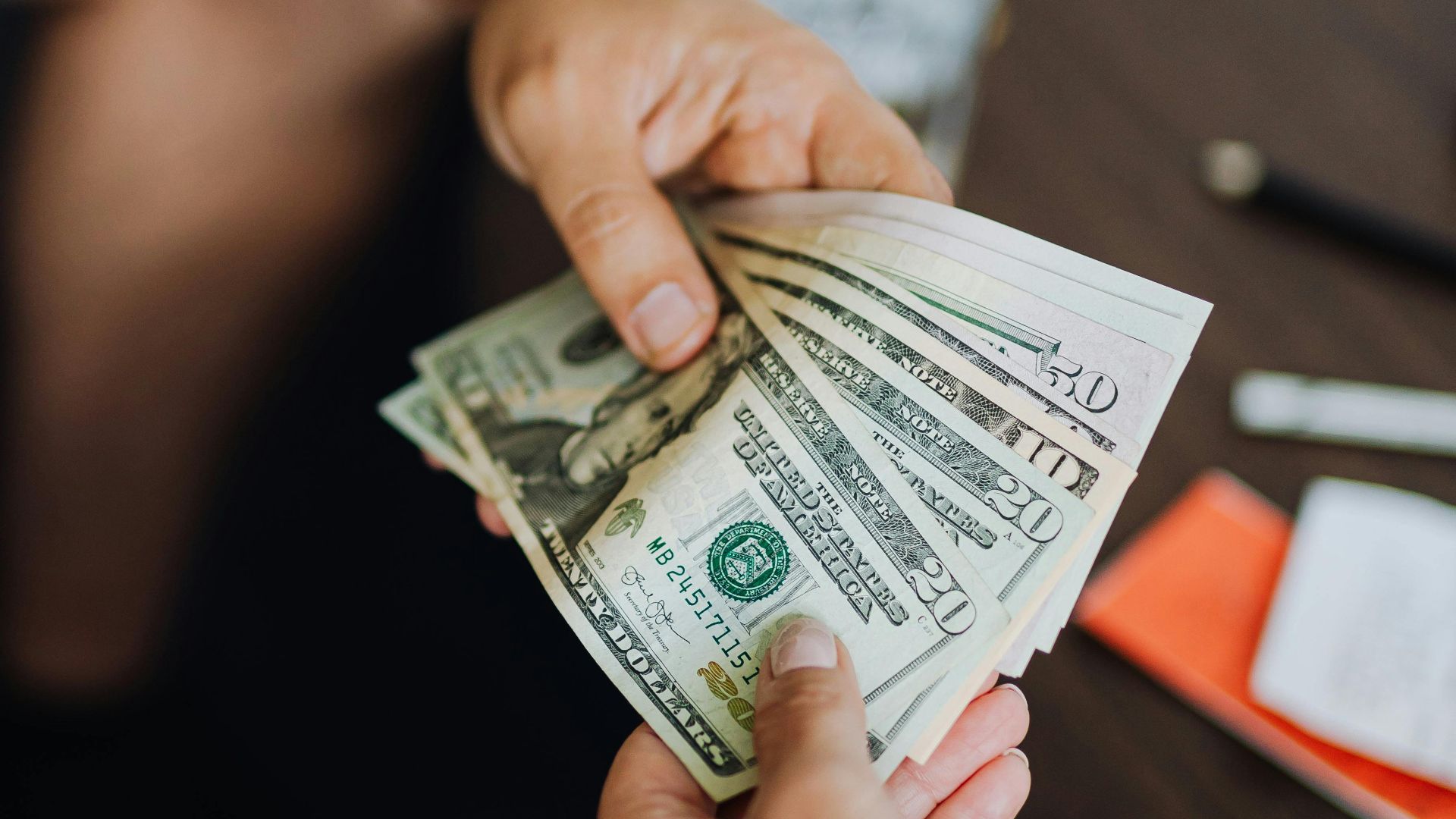 A close-up view of hands exchanging dollar bills indoors, symbolizing payment.