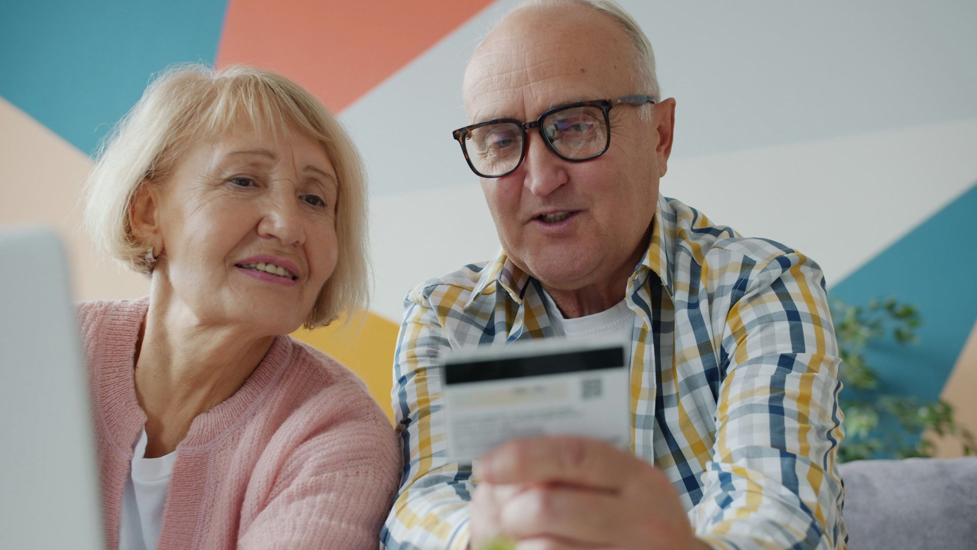 Elderly couple looking at credit card and laptop.