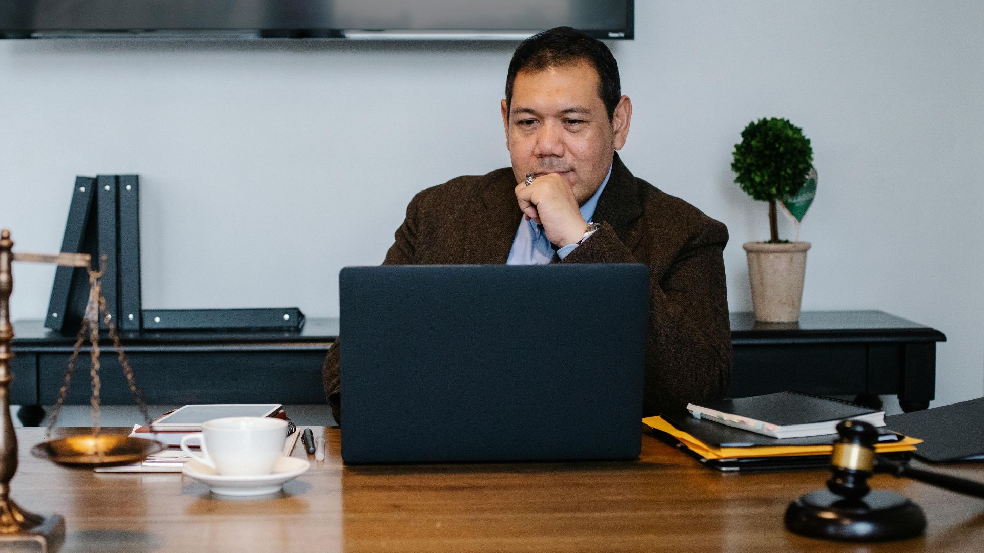 Serious ethnic mature man in formal outfit working with netbook at table with gavel