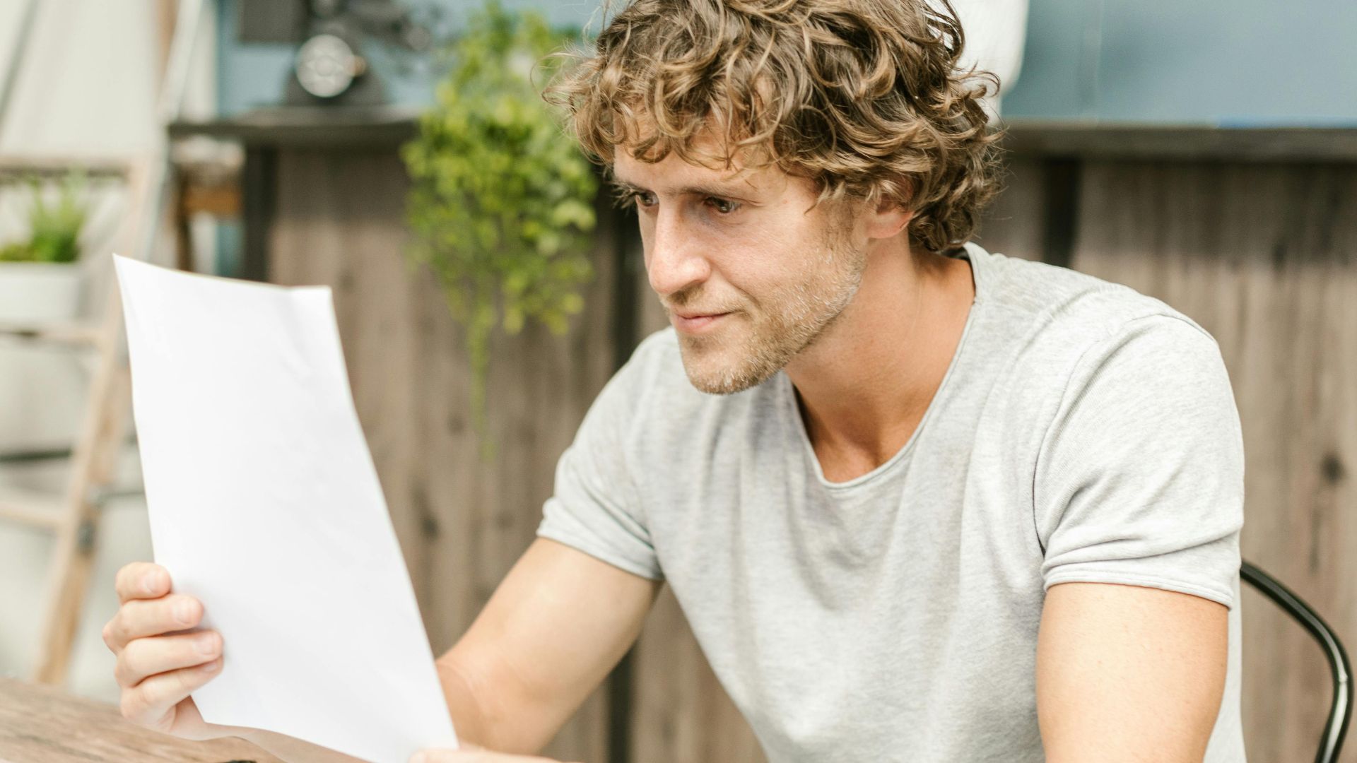 A man with curly hair evaluates documents at a desk, highlighting focused work in a professional setting.