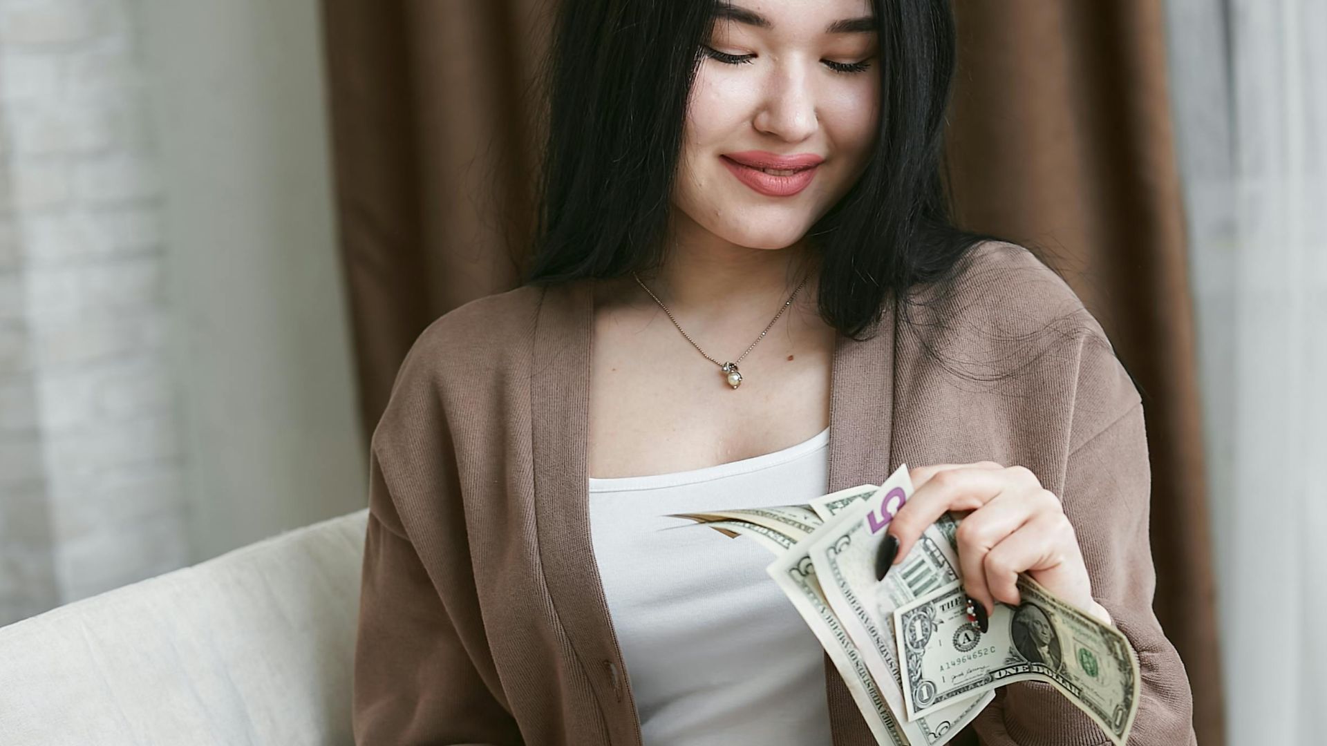 Asian woman happily counting US dollars, symbolizing financial planning and success.