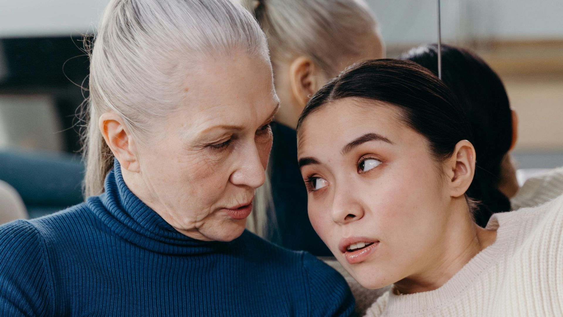 An elderly woman and a young woman share a tender moment while reading together indoors.
