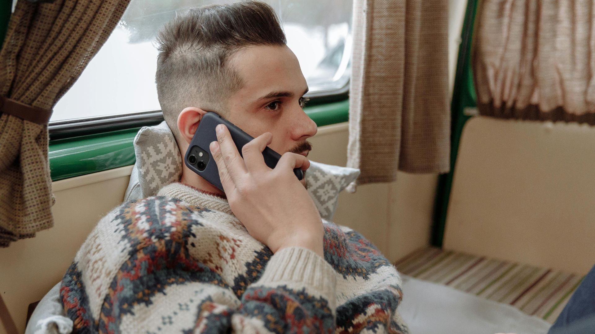 Casual adult man wearing sweater, relaxing indoors while talking on phone.