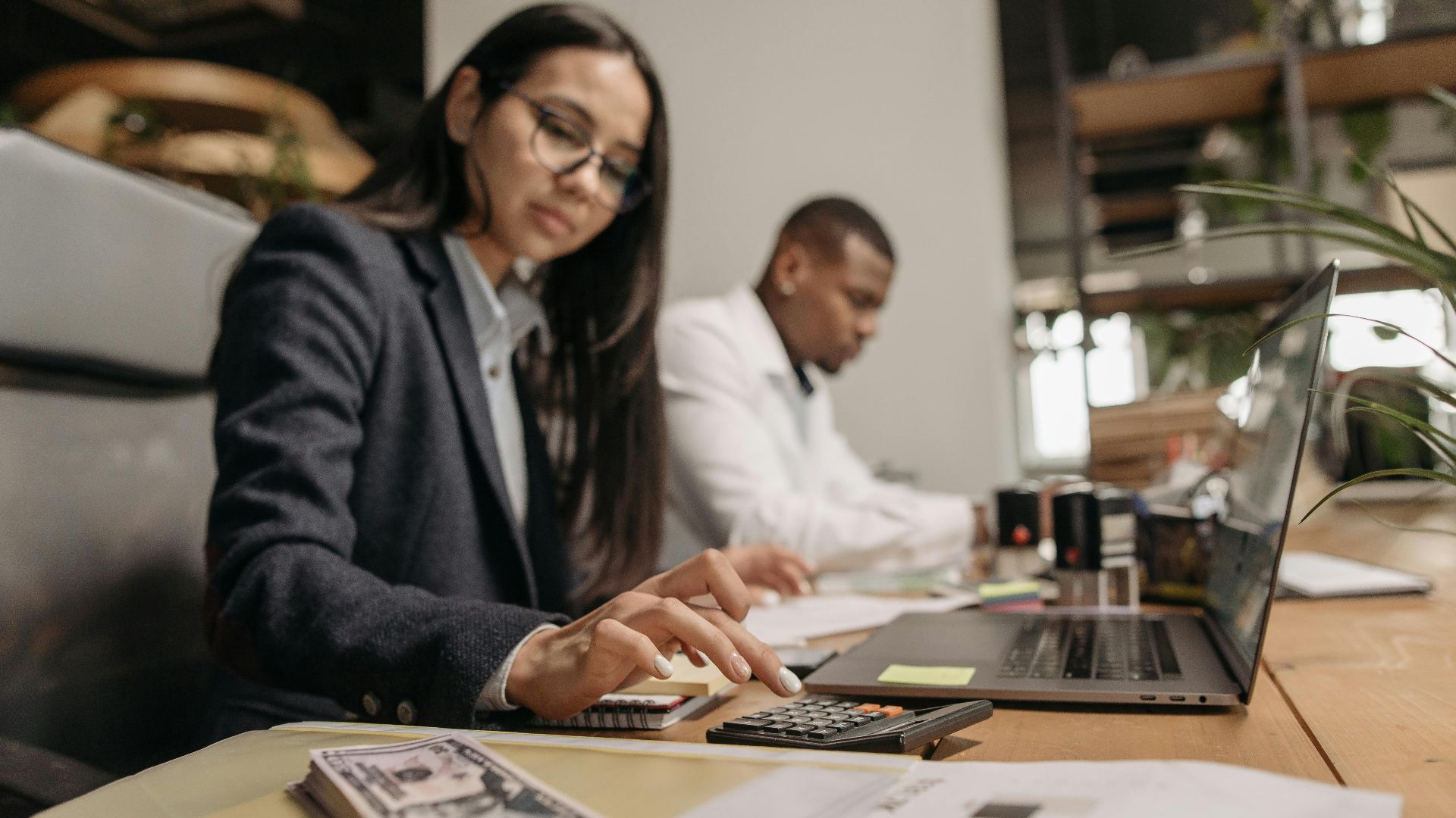 Two business professionals collaborating with a laptop and calculator in a modern office.