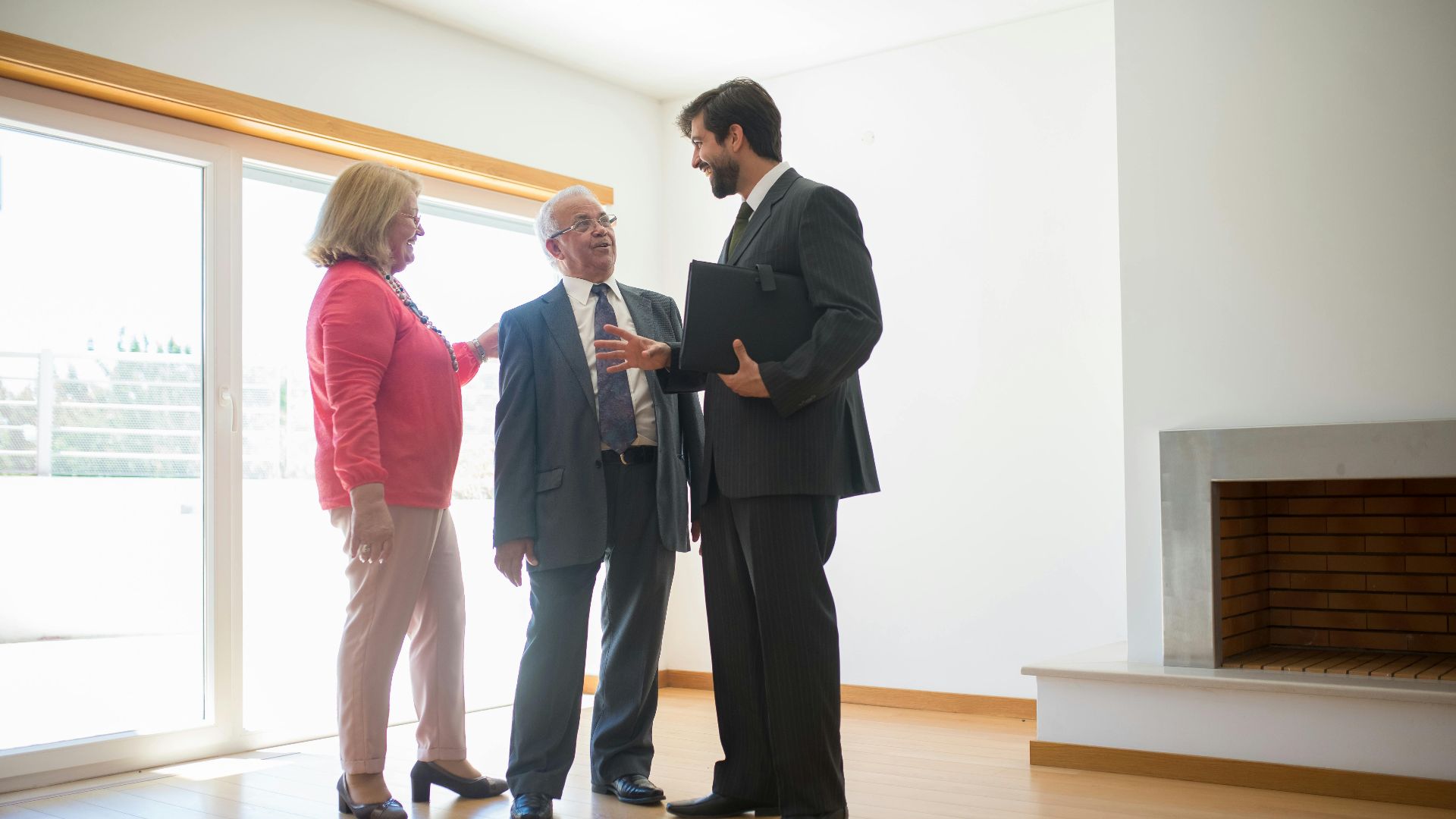 A real estate agent shows an empty house to senior clients, highlighting the spacious room.
