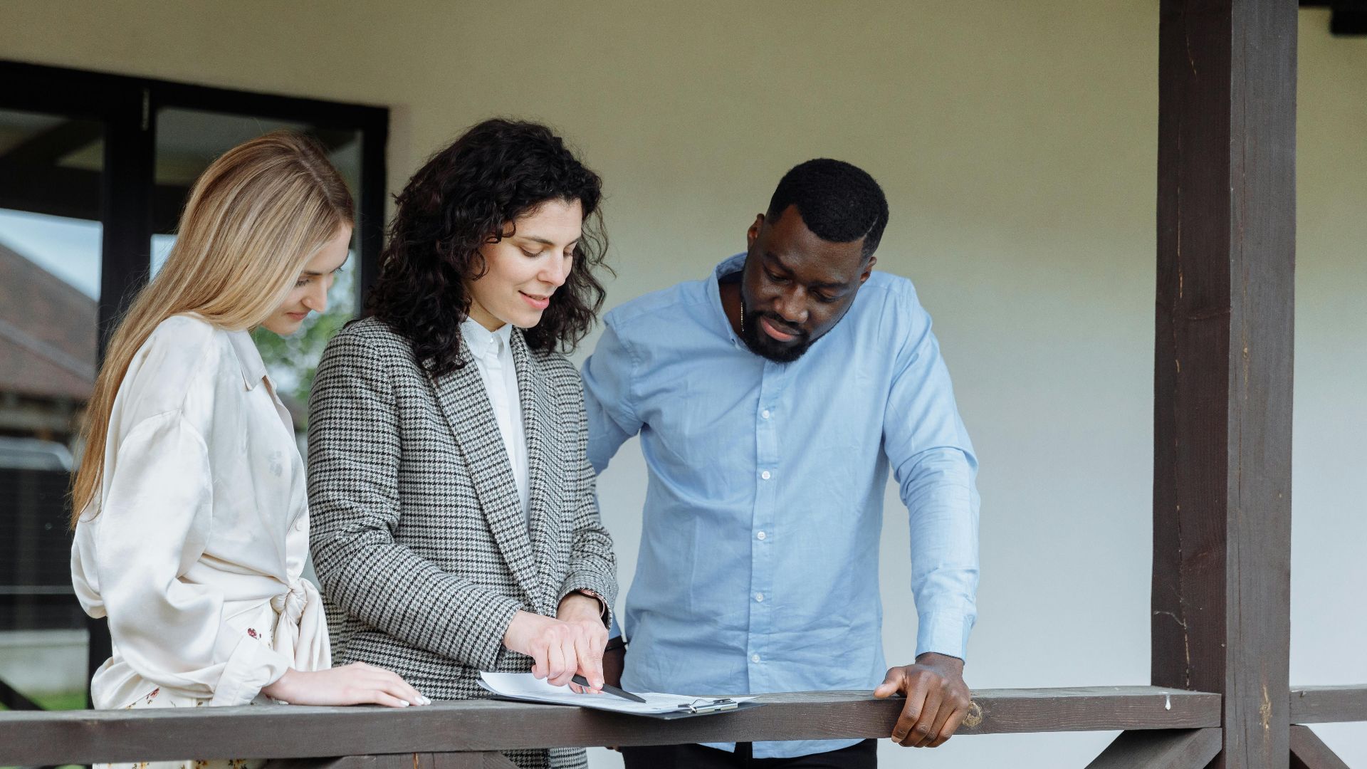 Real estate agent discussing property paperwork with a couple on a porch.