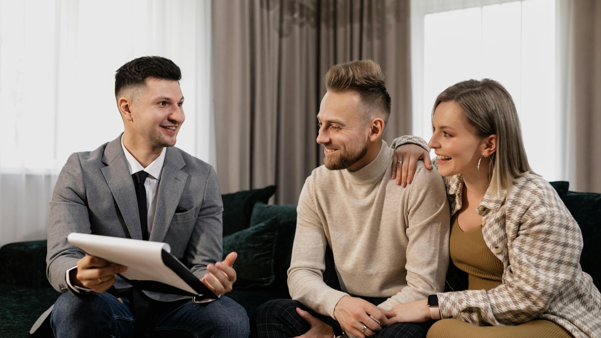 Real estate agent consulting a smiling couple on a couch in a cozy, indoor setting.
