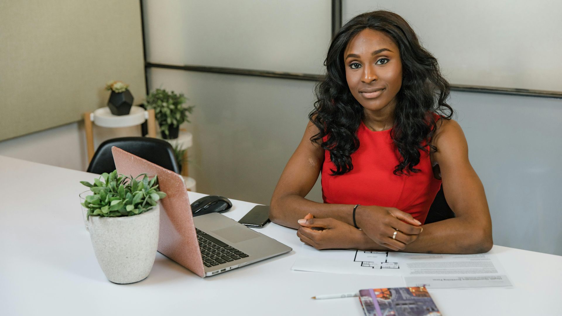 Professional woman sitting at a desk with laptop, papers, and plants in a modern office.