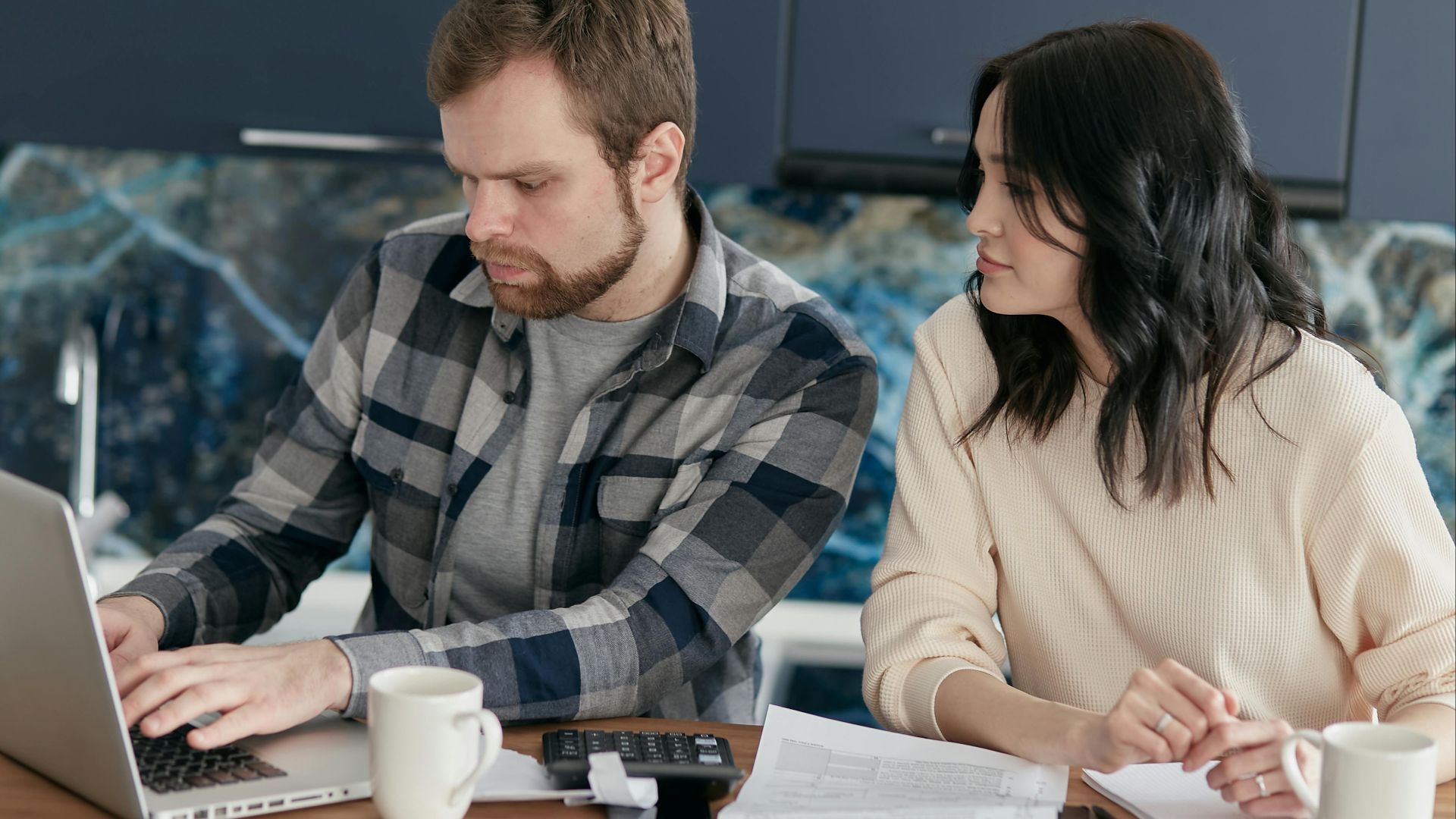 A couple working together on financial planning at home, using a laptop and paperwork.