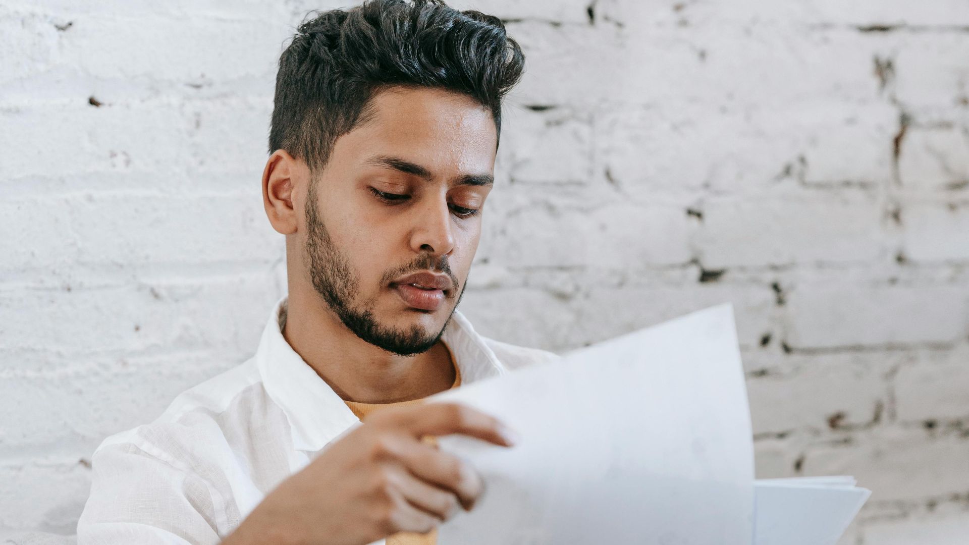 Concentrated young bearded Hispanic male sitting in armchair and analyzing contract while getting job offer