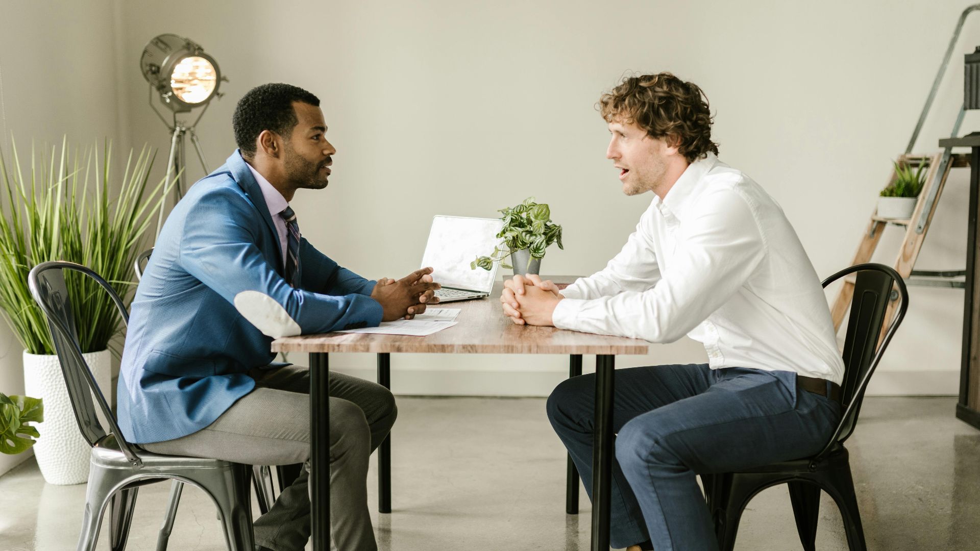 Two businessmen engaged in a professional discussion at an indoor office setting with greenery and modern decor.