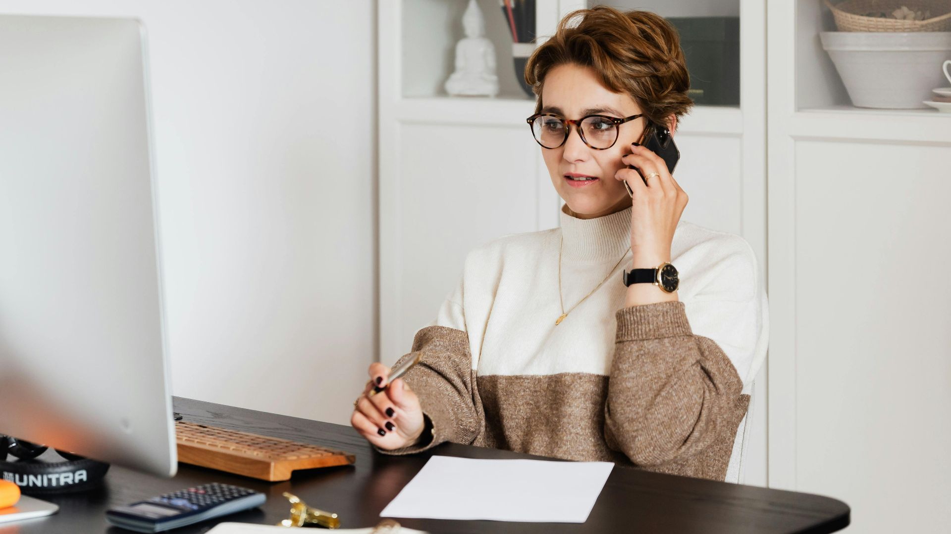 Smart confident female managing director listening to employees report on smartphone while working on computer in light modern office